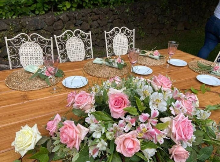 Mesa con centros de flores rosa pastel y sillas blancas decoradas